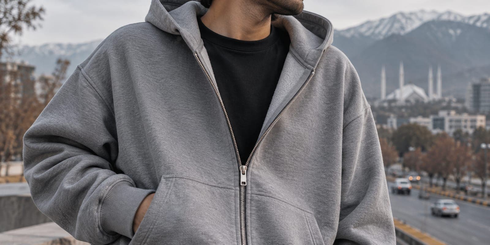 Close-up of a grey fleece zip-up hoodie worn open over a black cotton tee on a winter street