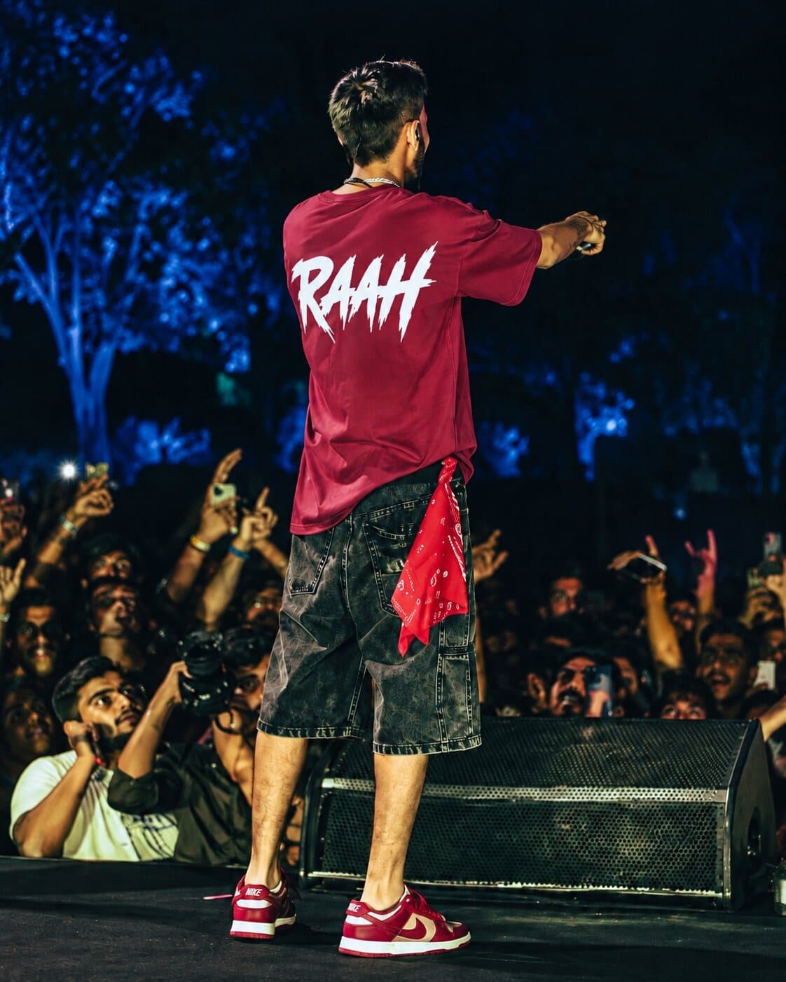 Talha Anjum on stage in Lahore wearing the RAAH maroon tee, back view facing the crowd